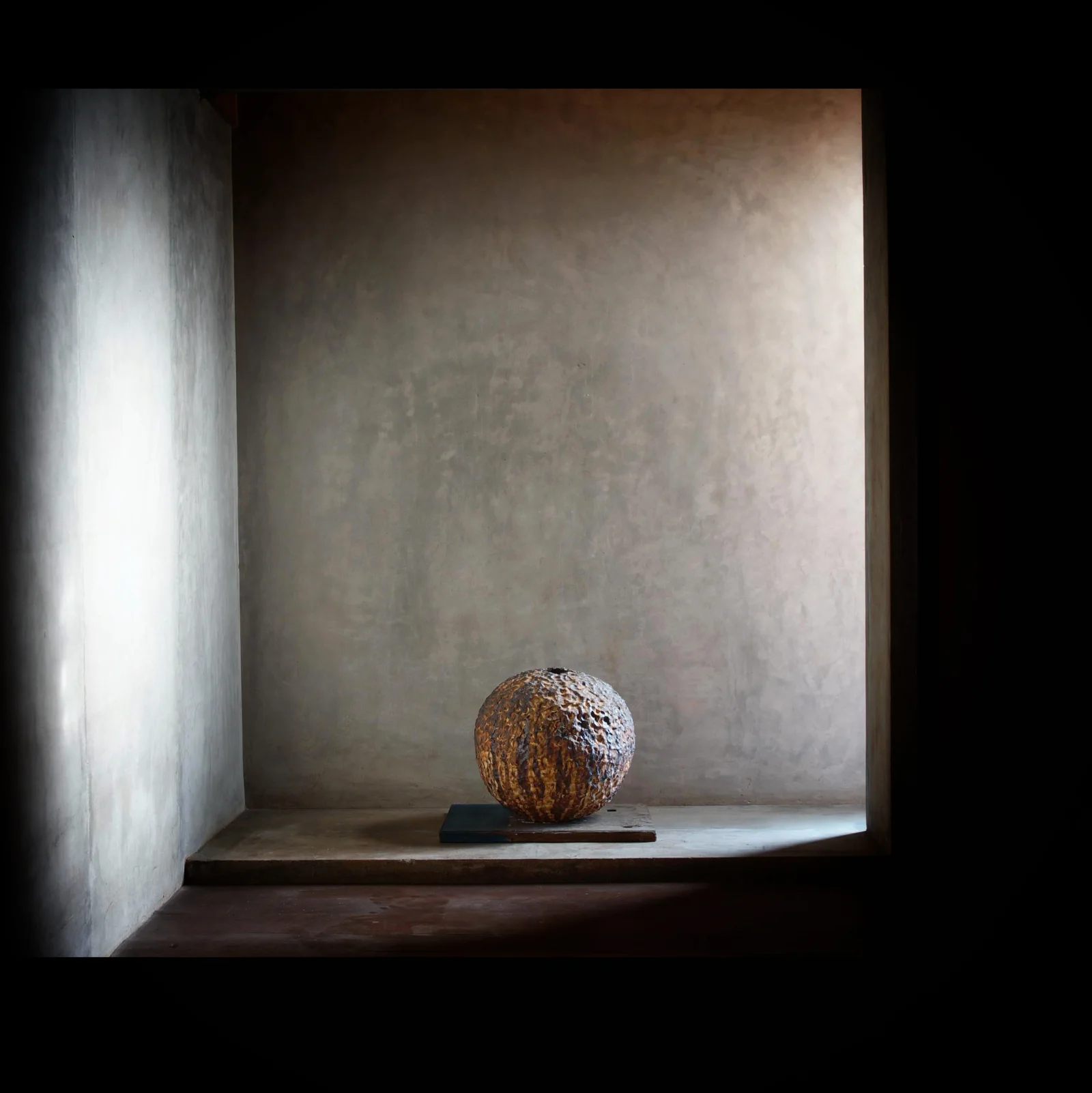 A textured spherical sculpture displayed within a deep architectural recess