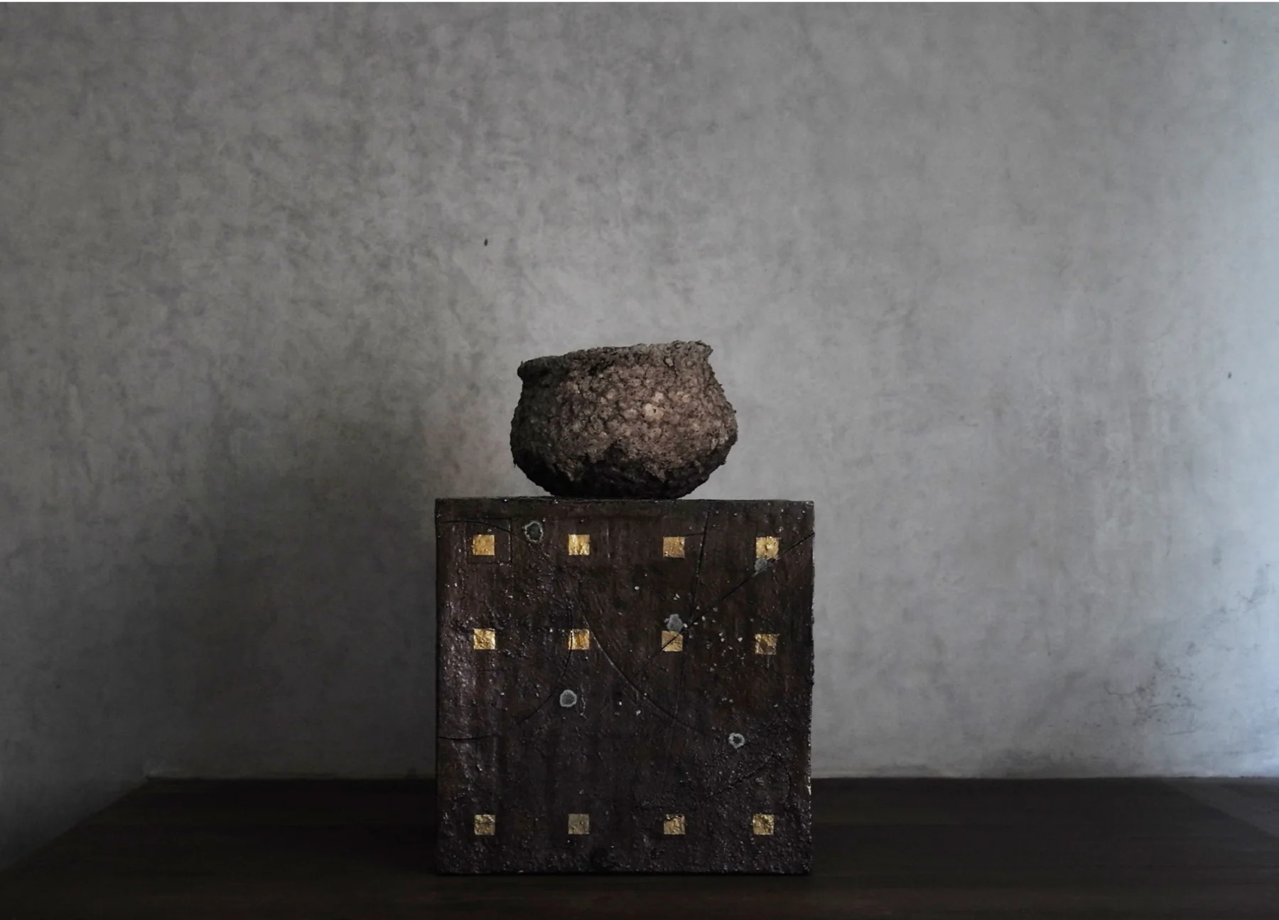 A hand-built ceramic vessel displayed on a dark sculptural plinth