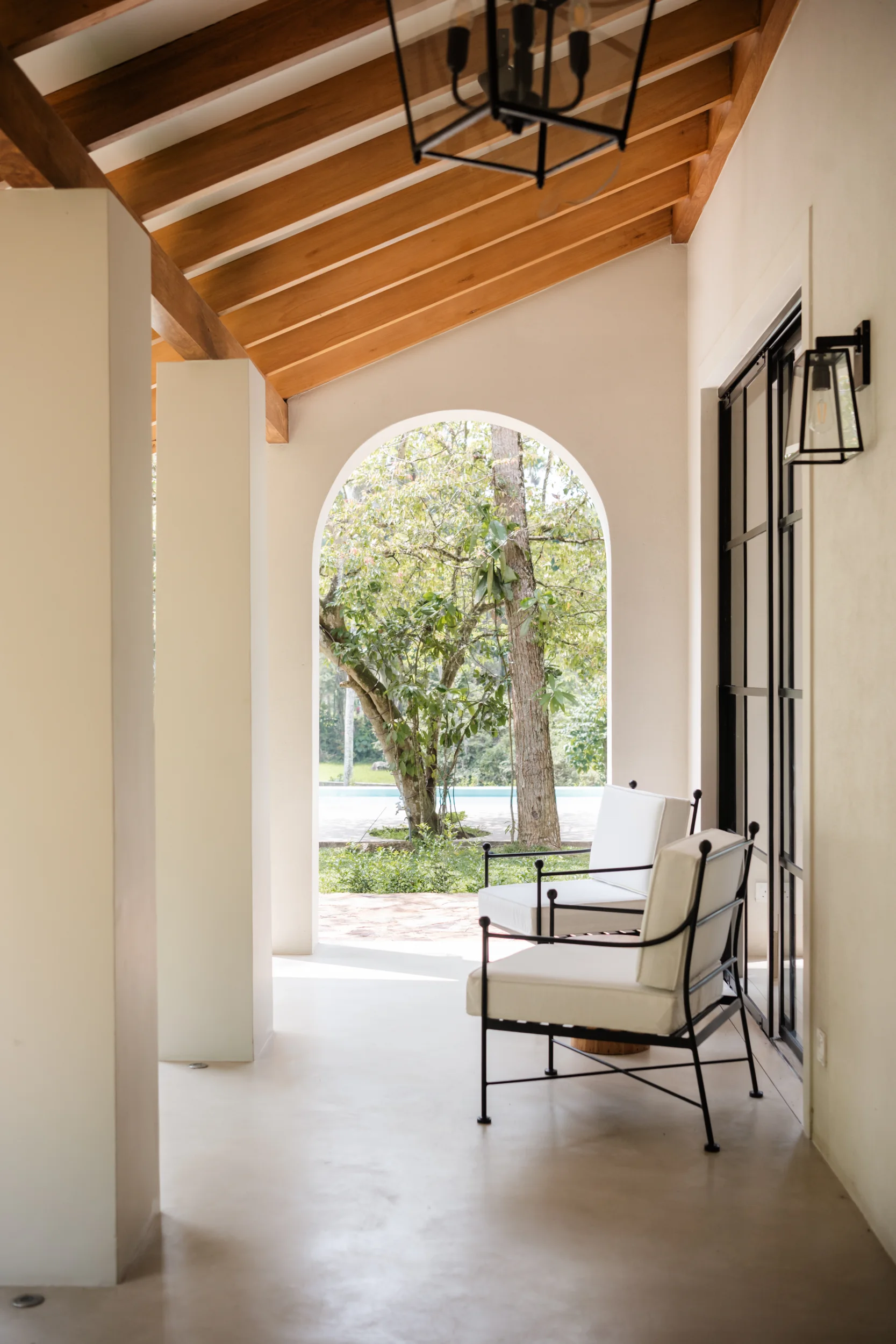 Covered Sa House verandah with timber roof, white lounge chairs and a garden view