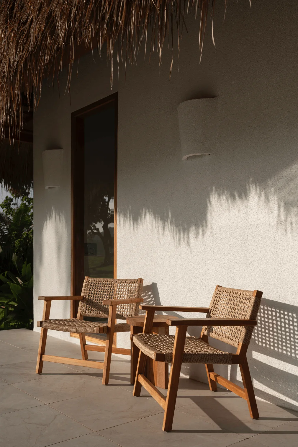 Two timber-and-woven chairs beneath a deep thatched terrace at The Sanubari