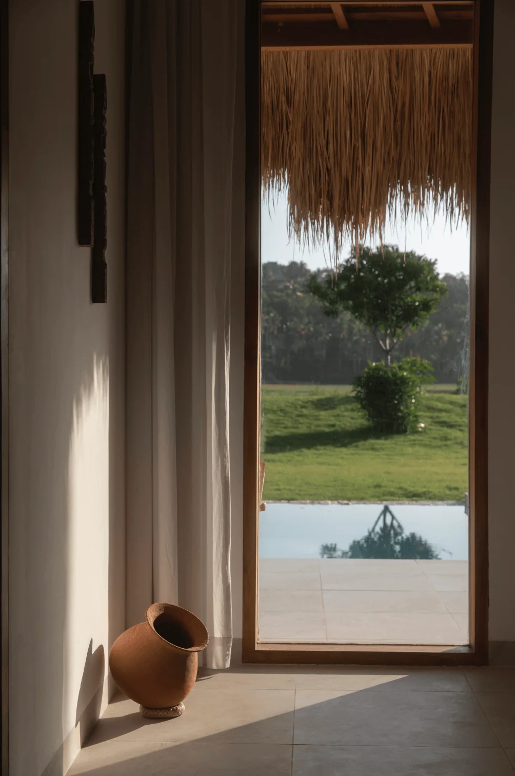 A clay vessel and garden pool seen through a tall timber-framed opening