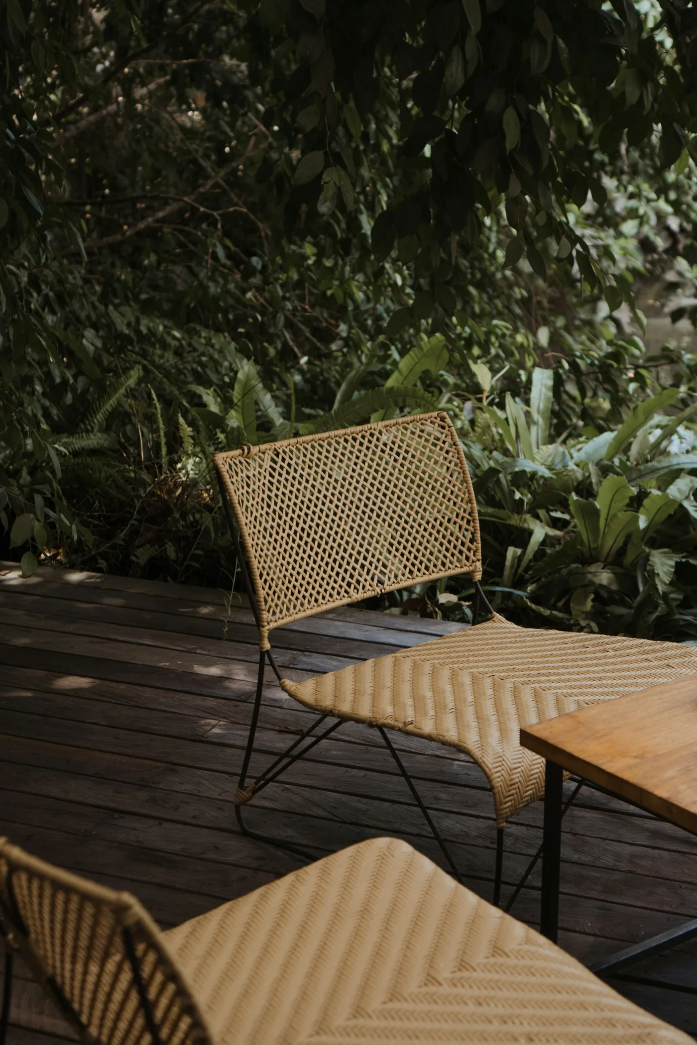 Rattan chairs and a timber table on a compact tropical deck surrounded by greenery