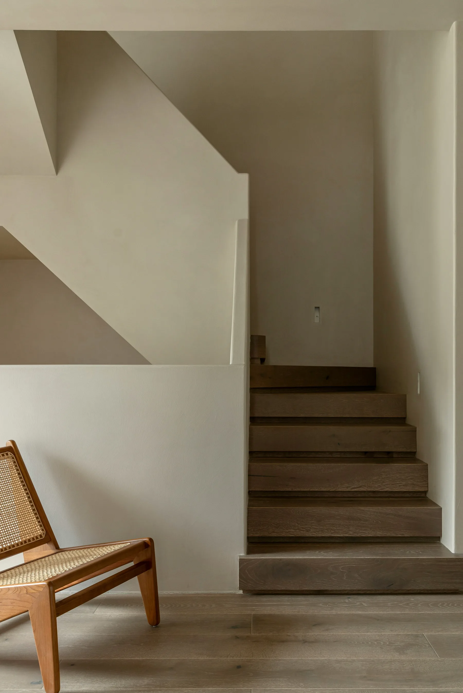 Minimal tropical interior with timber stairs, soft plaster walls, and a woven chair