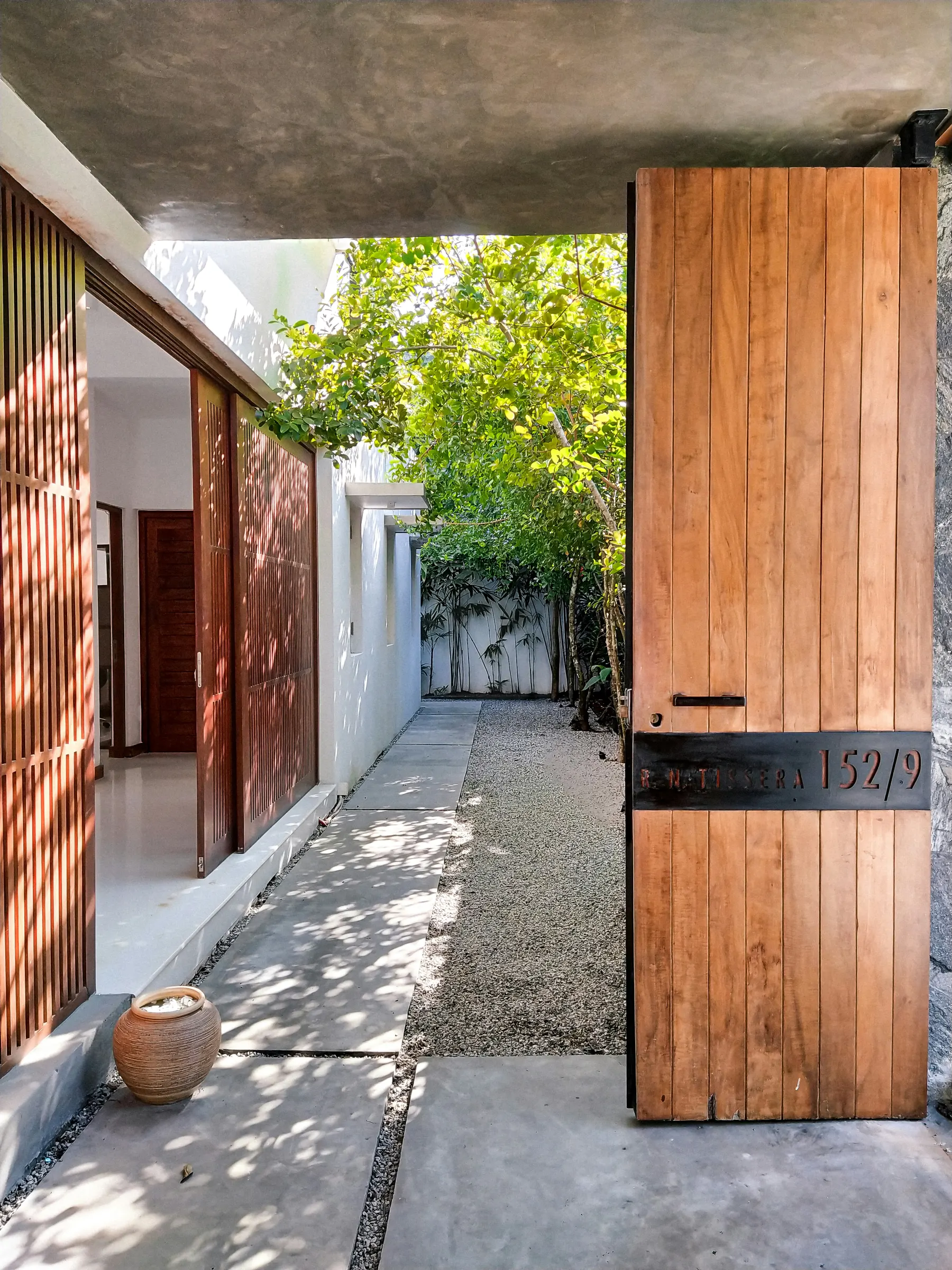 A tall timber door opening to a shaded tropical path and garden