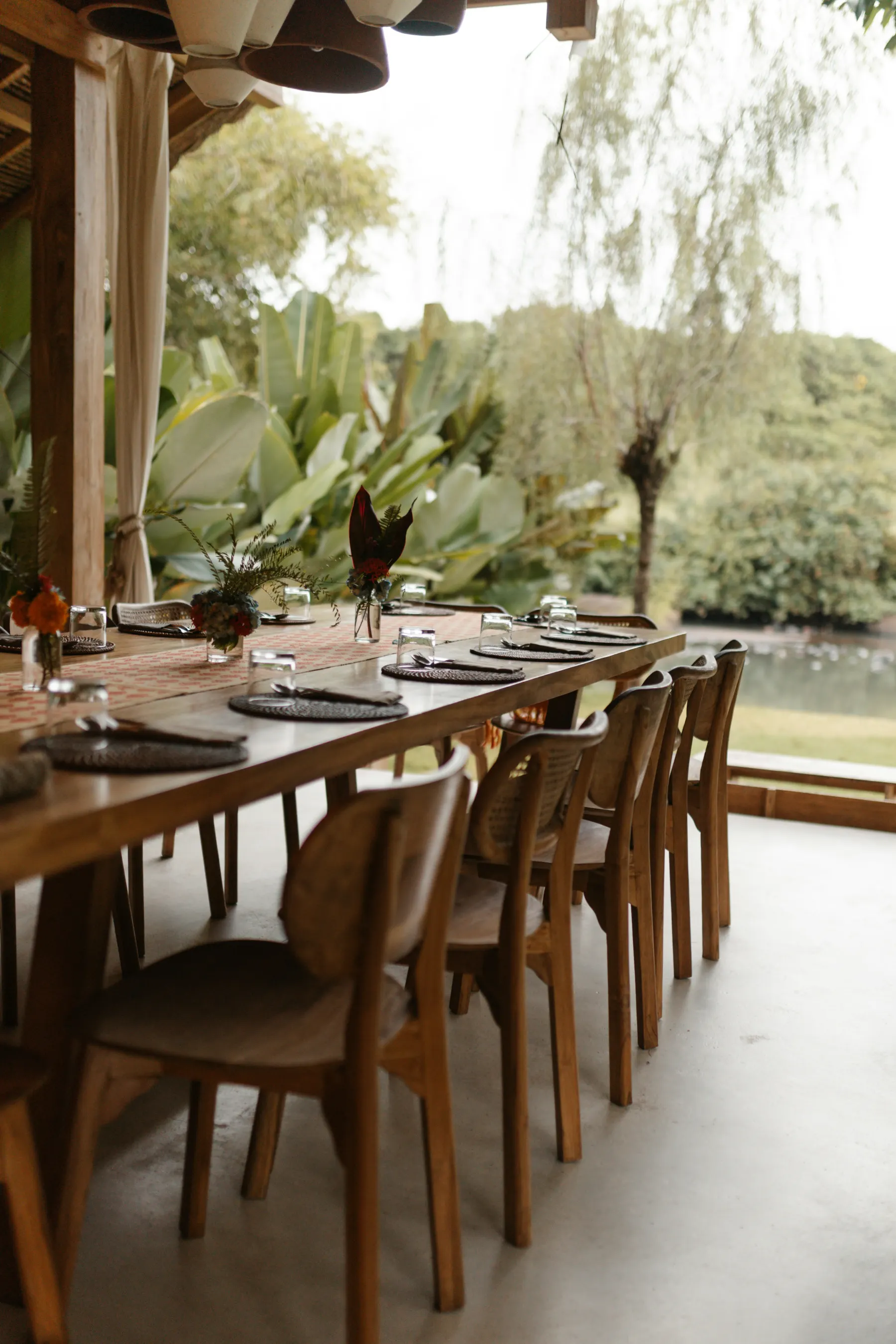 A shaded open-air dining terrace facing tropical landscape and water