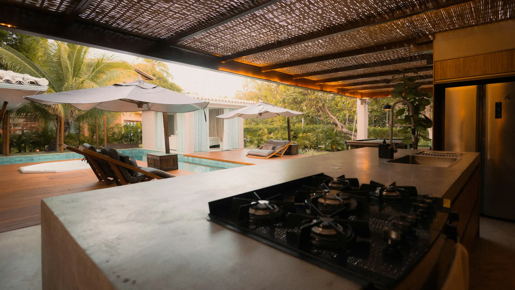 An open kitchen flowing directly to a shaded pool terrace and garden
