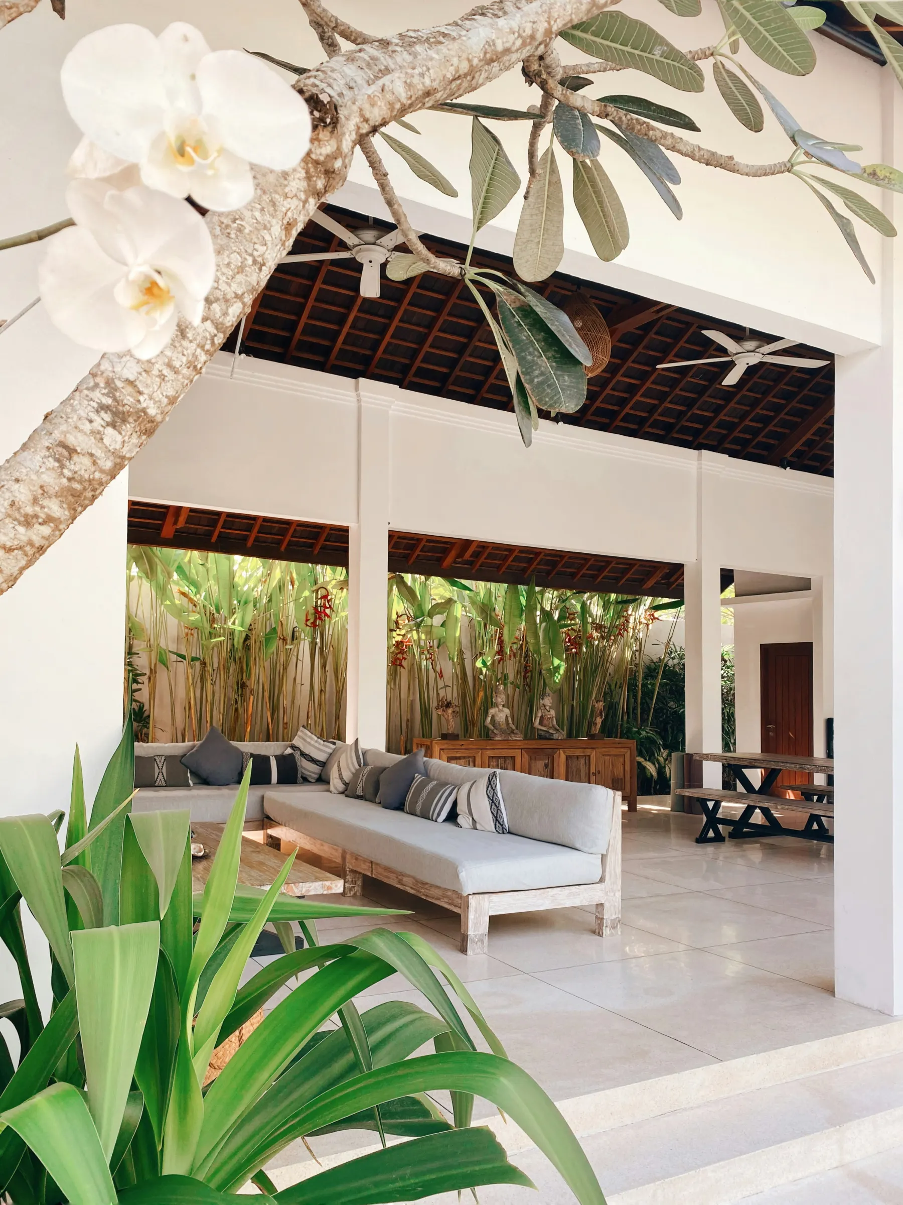 An open tropical veranda living room framed by greenery, shade, and fans